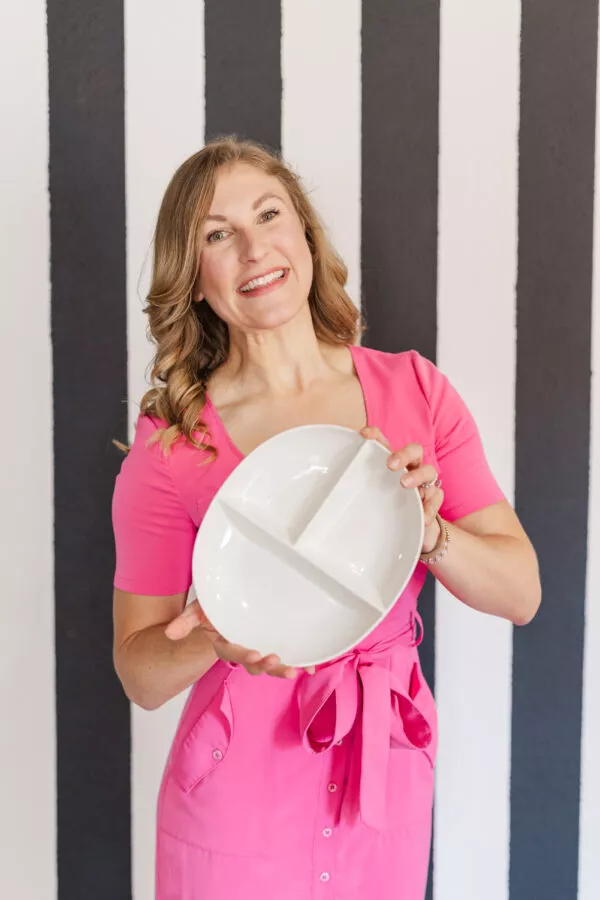 Registered dietitian in a bright pink dress holding a white portion plate, representing balanced eating and personalized nutrition at Whitness Nutrition.